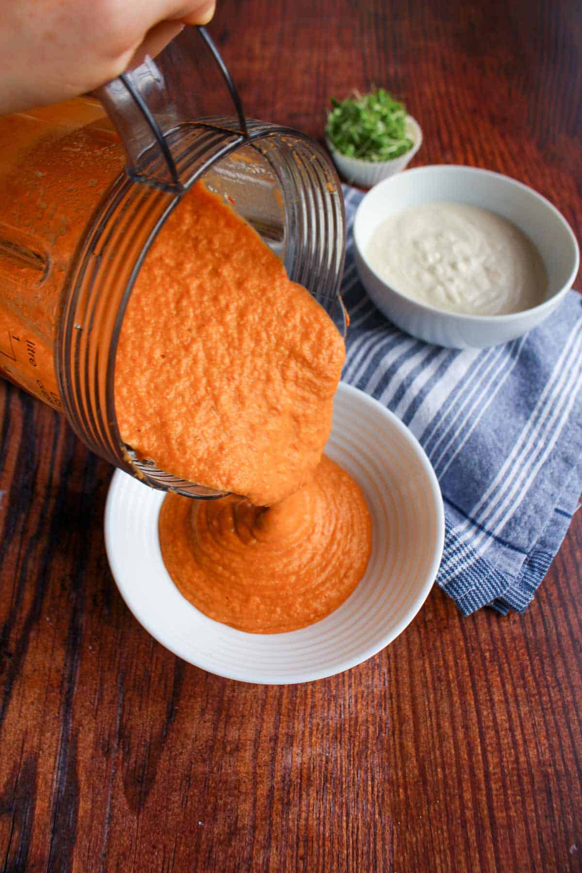 Pouring the chickpea soup with vegetables into a bowl with cashew cream behind it in another dish.