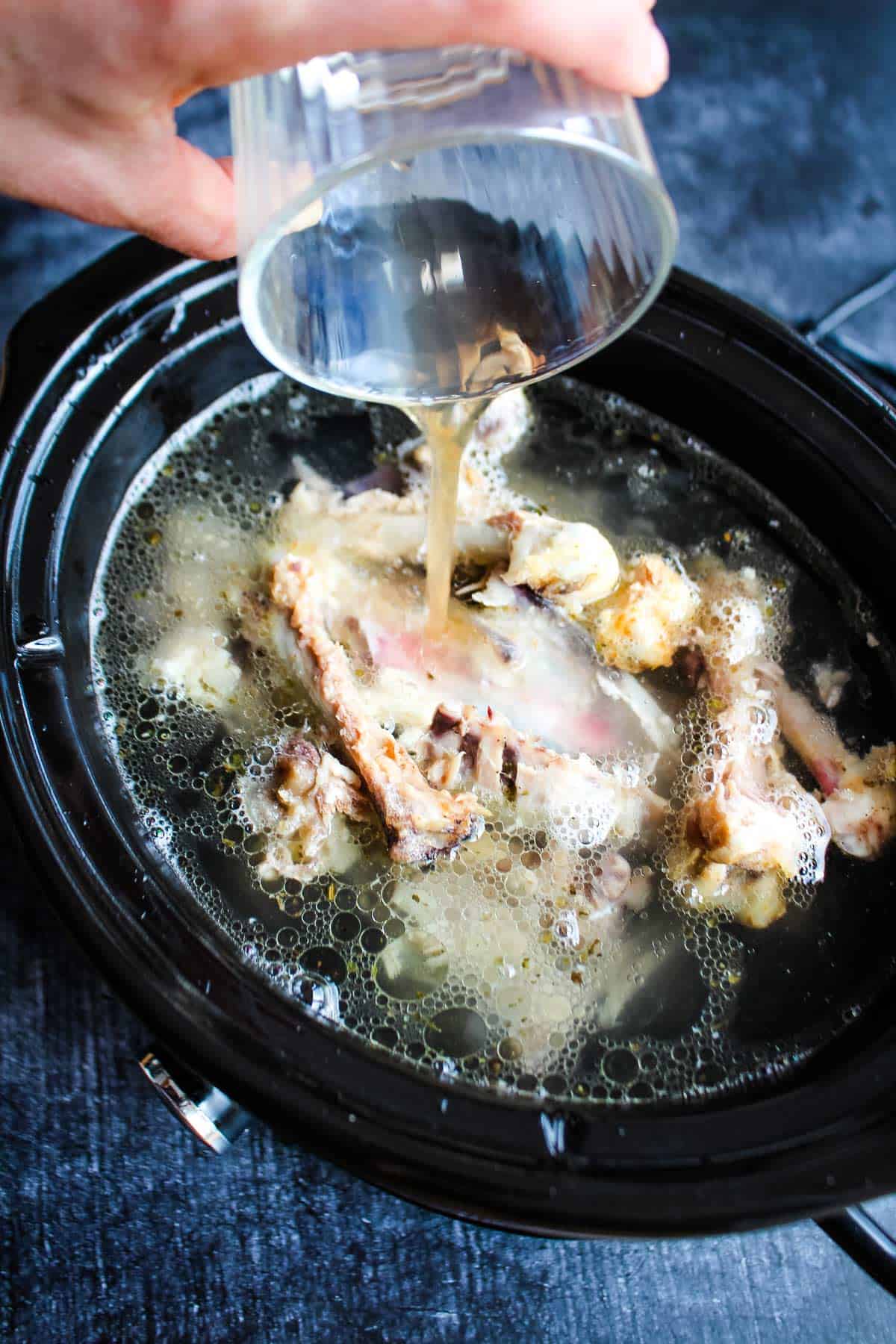 Adding apple cider to the bone broth in the slow cooker.