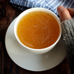 A cup of chicken bone broth with a hand cupping it to sip.