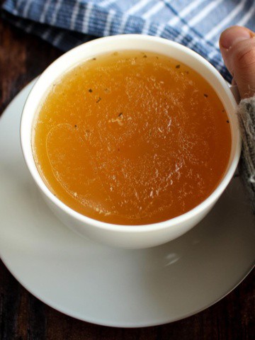 A cup of chicken bone broth with a hand cupping it to sip.