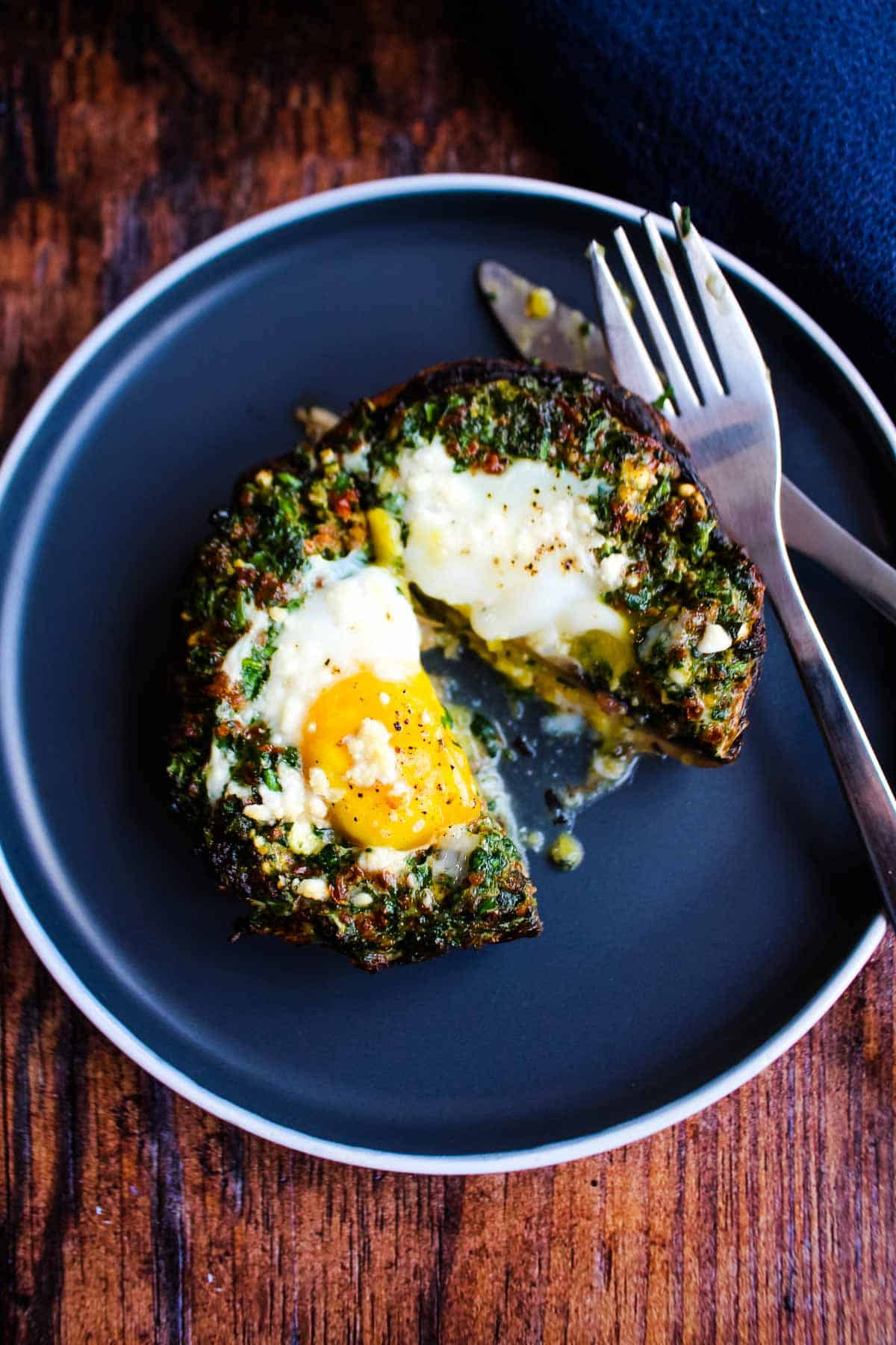 A breakfast mushrooms stuffed with eggs and veggies on a plate with fork and knife.