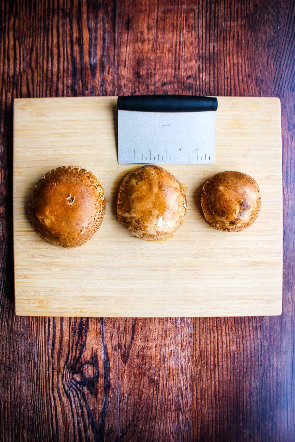 Image of three different sized mushrooms on a cutting board with a measuring tool.