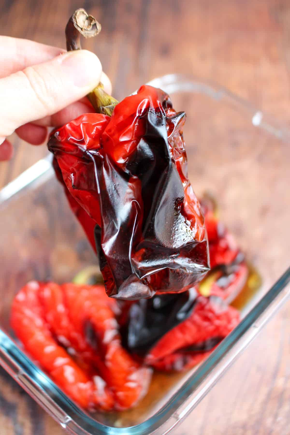 A hand holding a charred and wrinkled red bell pepper after being roasted.