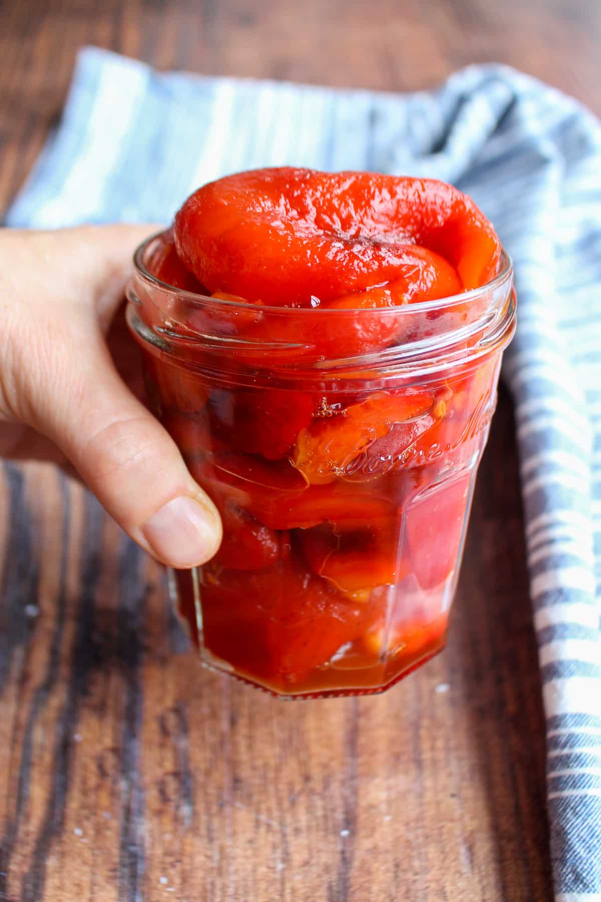 Hand holding a clear jar overfilled with roasted red peppers