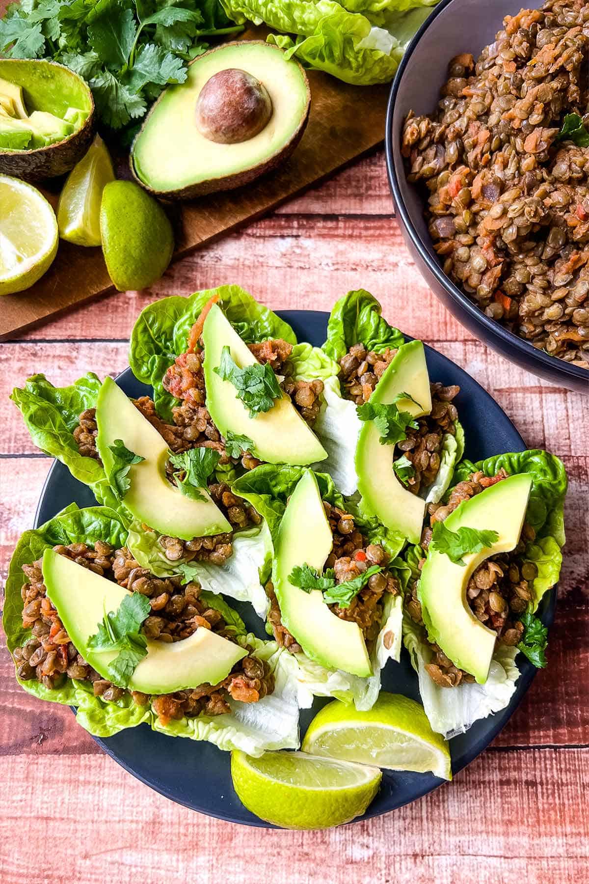  A plate of vegetarian lettuce wraps on the table with avocado and bowl of lentil meat in the top.