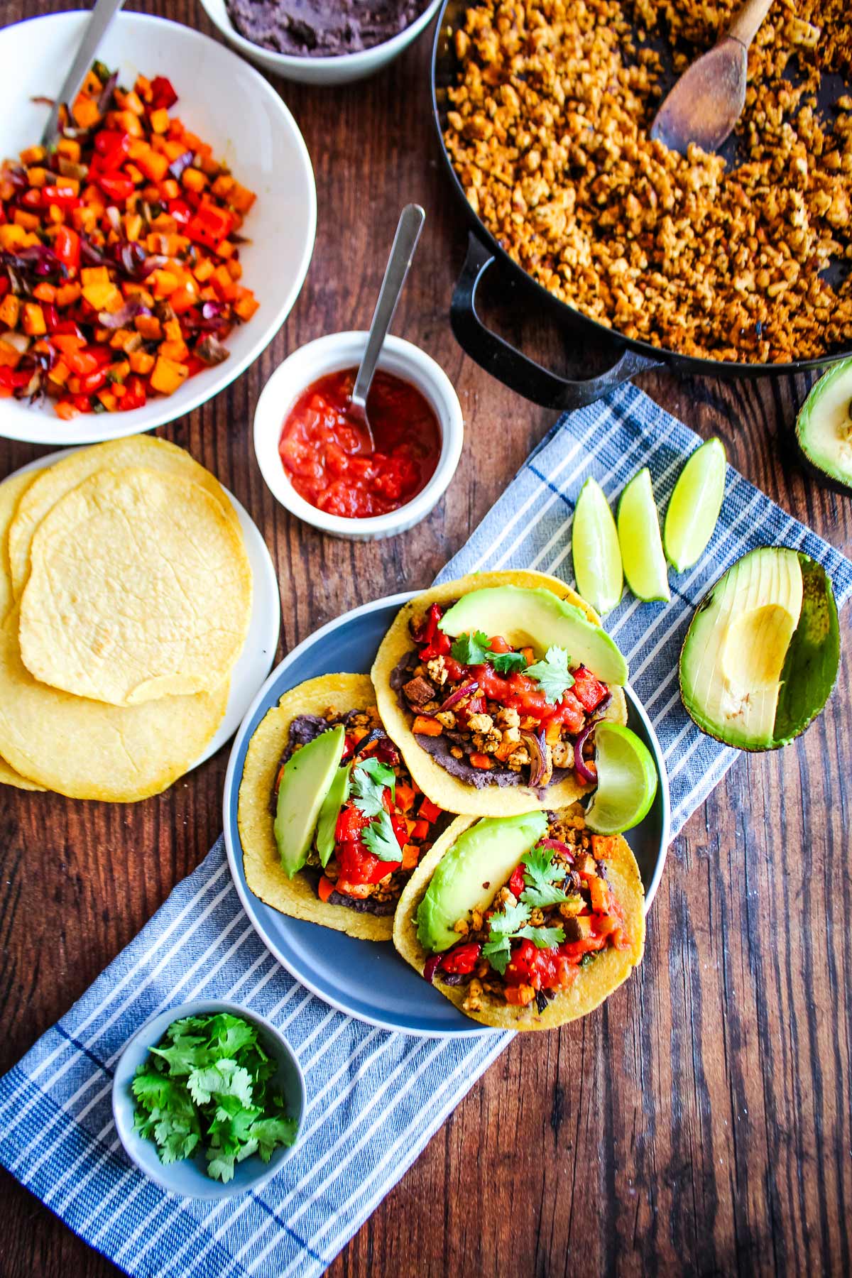 A plate with a three tempeh tacos on it and a skillet of chorizo tempeh and bowl of roasted veggies to the side.