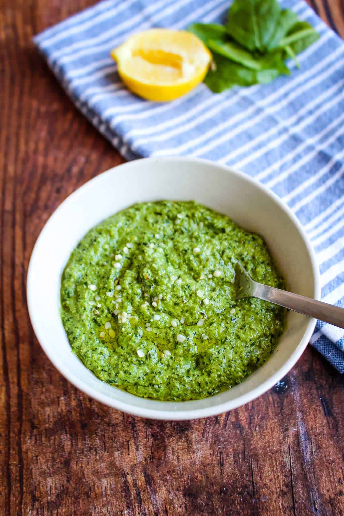 A bowl of spinach pesto on the table with a spoon in it. 