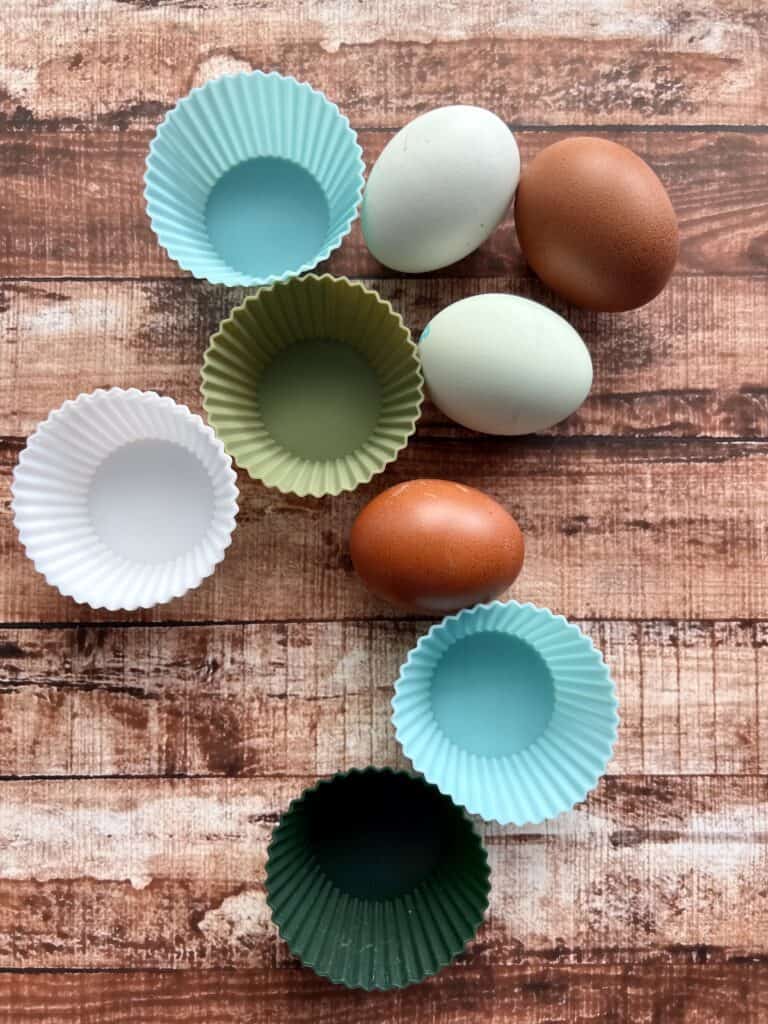 An assortment of different colored eggs alongside blue, white, and green silicone muffin liners