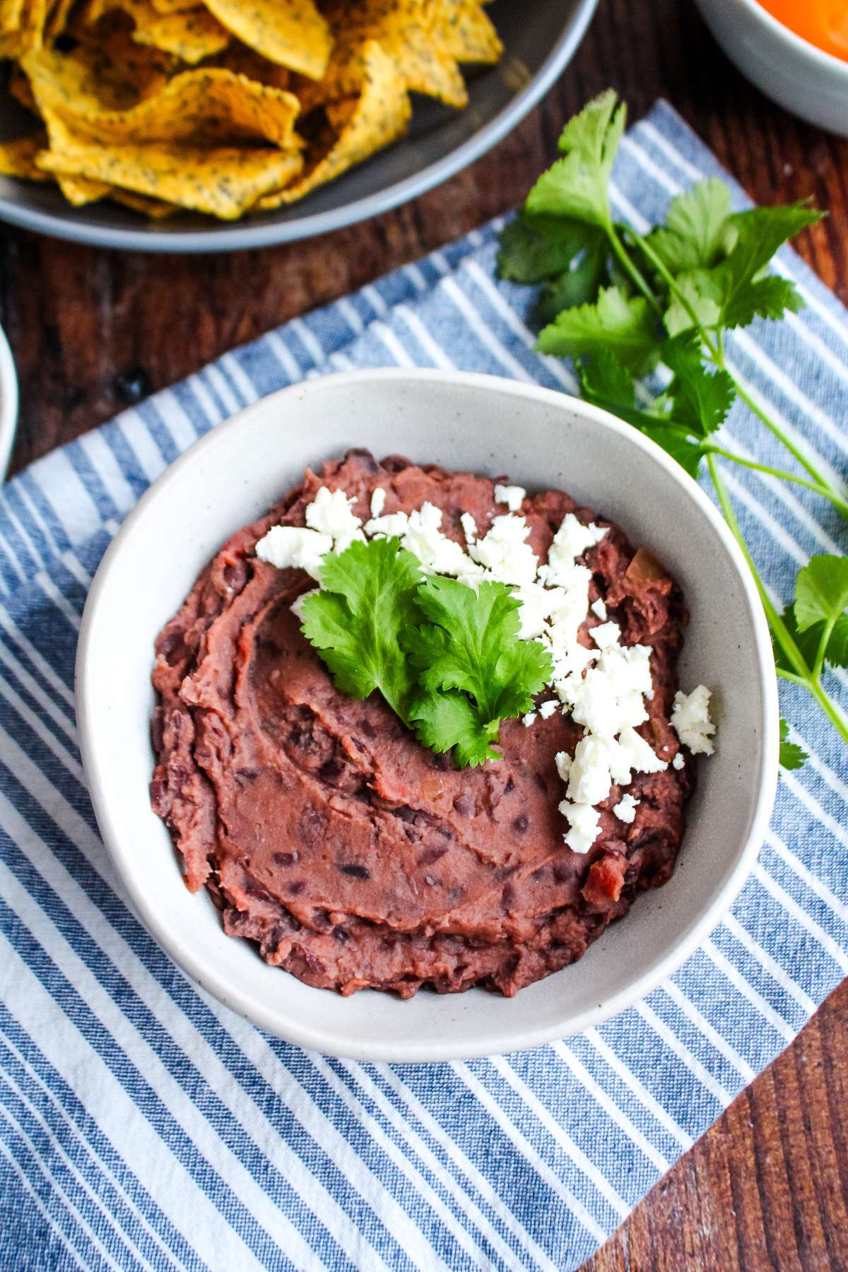 A bowl of black bean dip on the table with crumble cheese and cilantro on top.