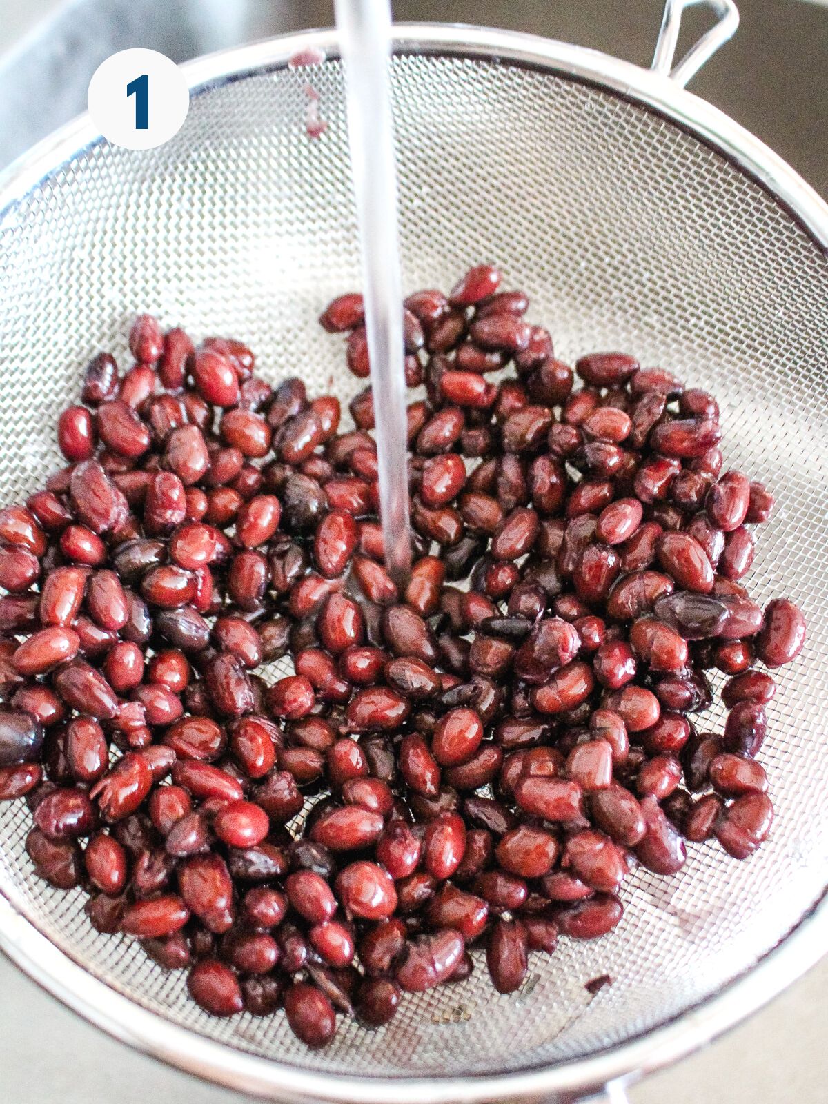 Black beans in a colander with water running over them to rinse.