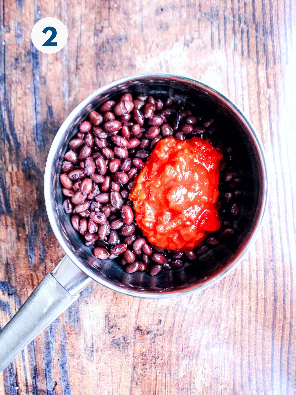 Black beans in a small saucepan with tomato sauce.