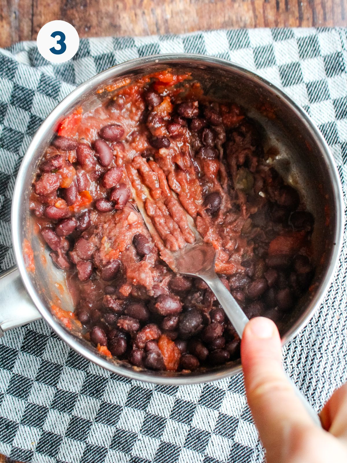 A fork mashing the black bean mixture in the pot.