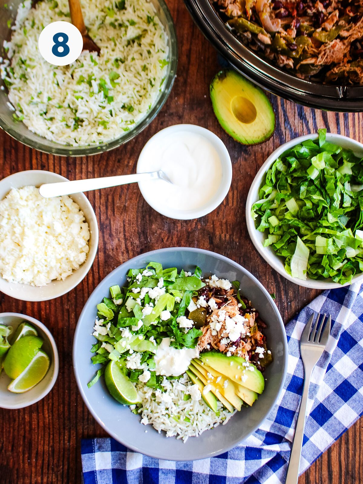 A shredded chicken taco bowl ready to eat on a table with extra toppings around it.