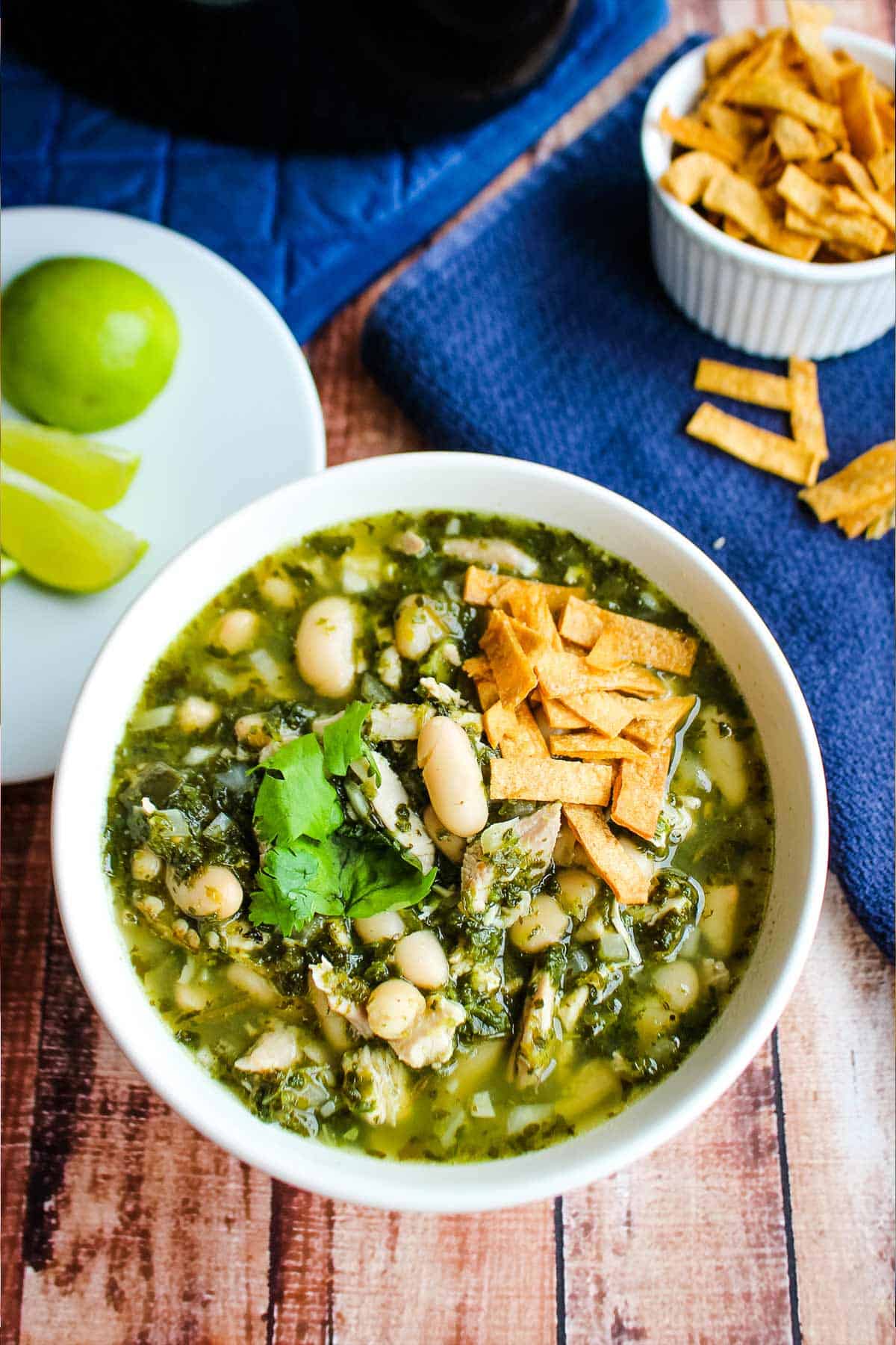 A bowl of spicy chicken soup on the table with tortilla chips on top.