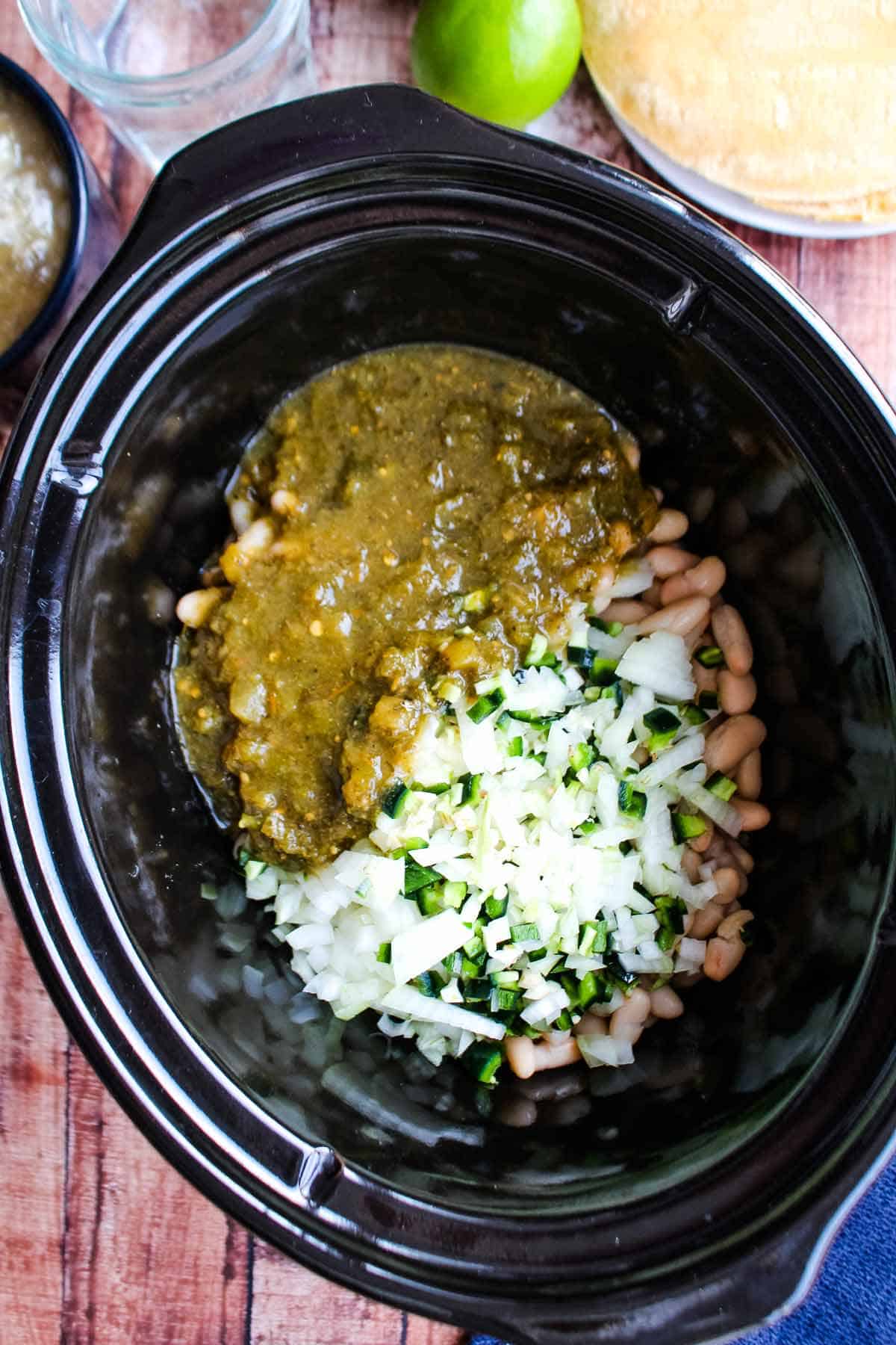 Onions, garlic and jalapenos along with the salsa verde added to the slow cooker on top of the beans and chicken.