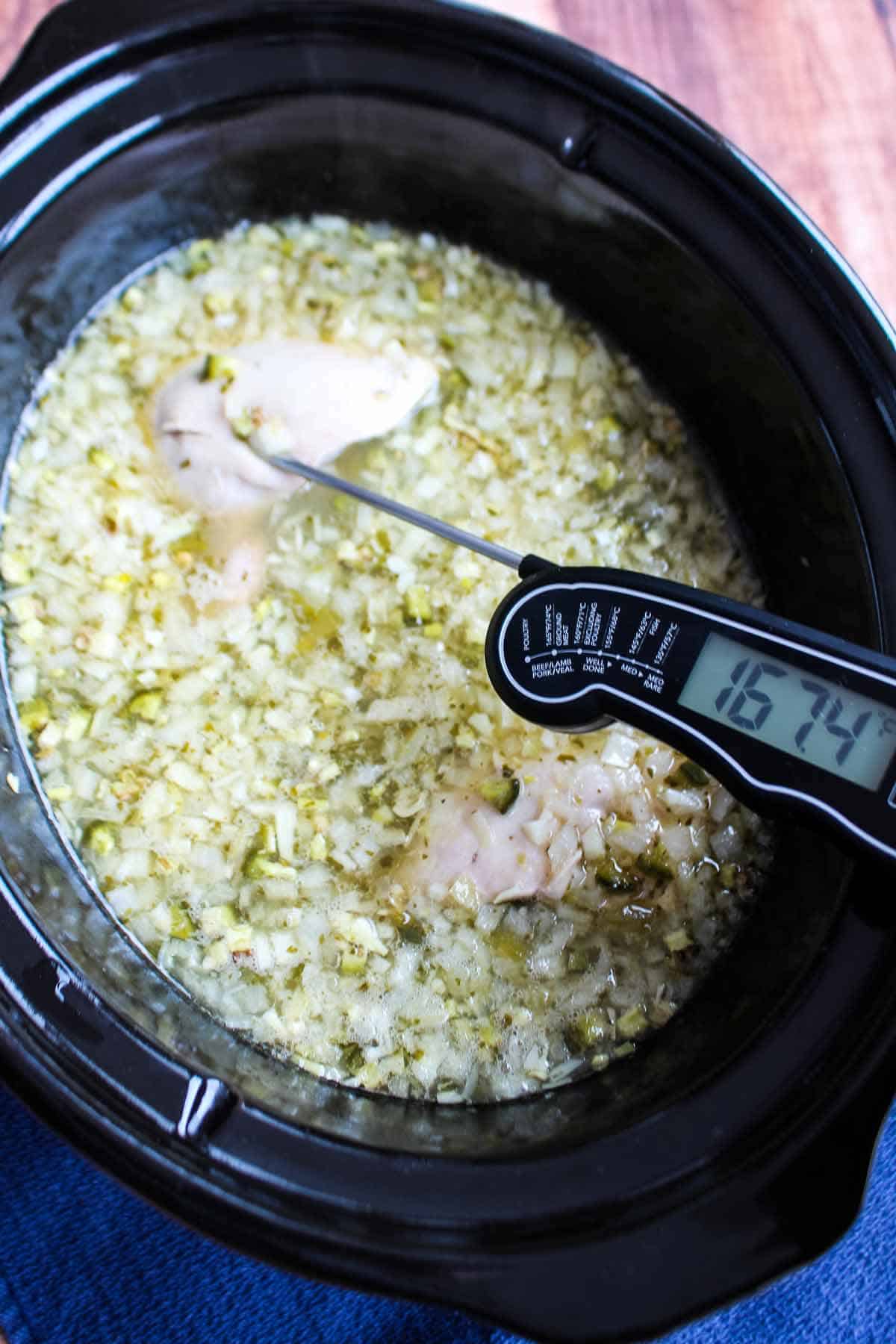 Spicy chicken soup cooking in a slow cooker and a thermometer checking the chicken for doneness.