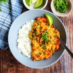 A bowl of red lentil stew in a gray bowl with some rice.