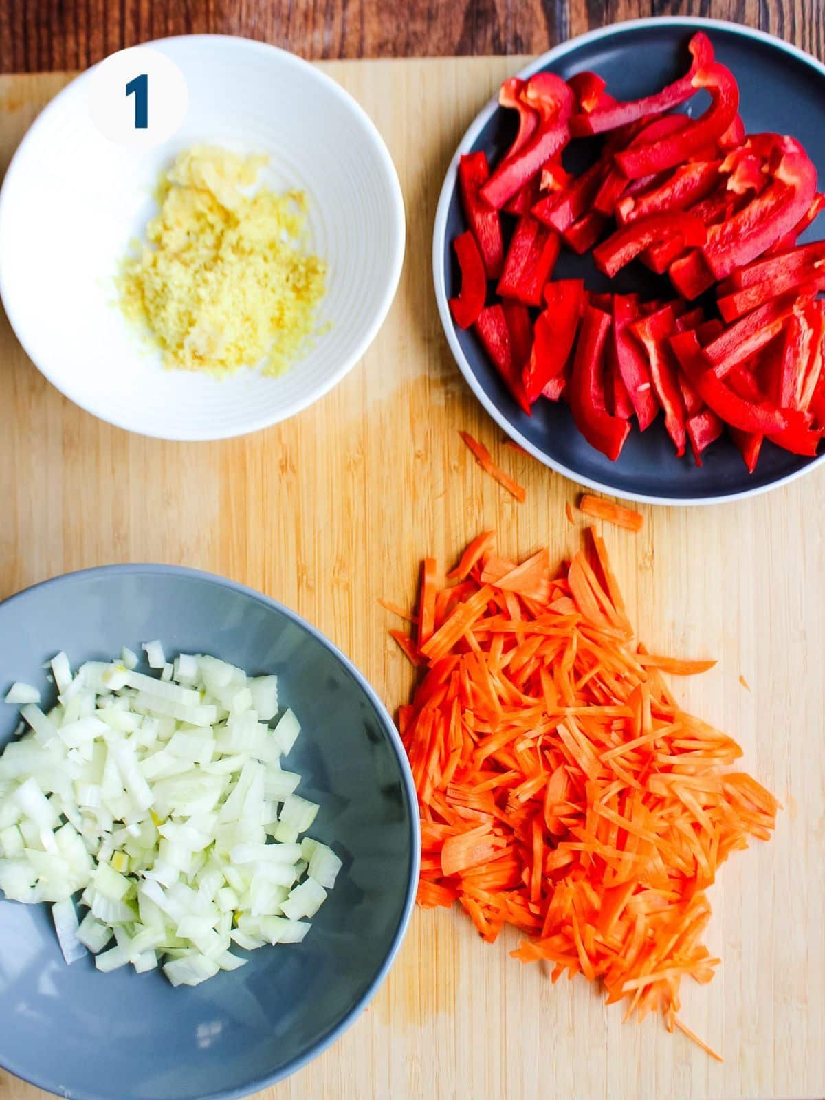 Vegetables prepped up in bowls on a cutting board.