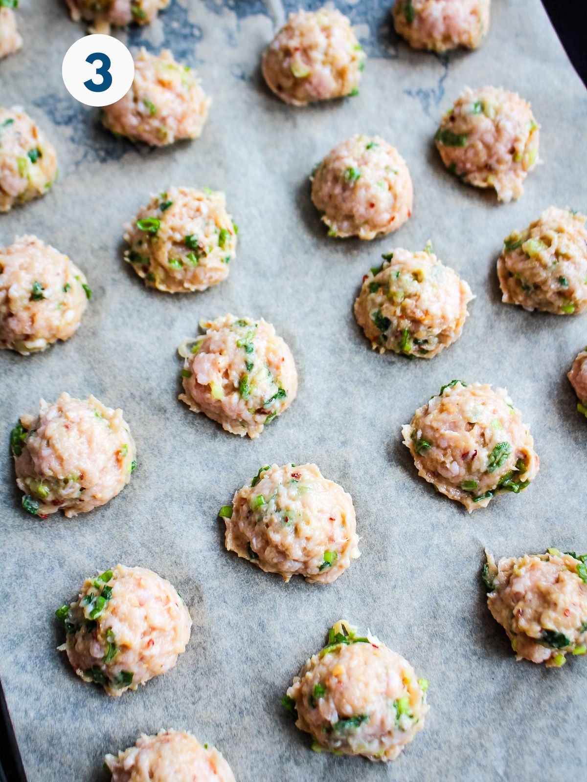 Meatballs scooped onto a baking pan.