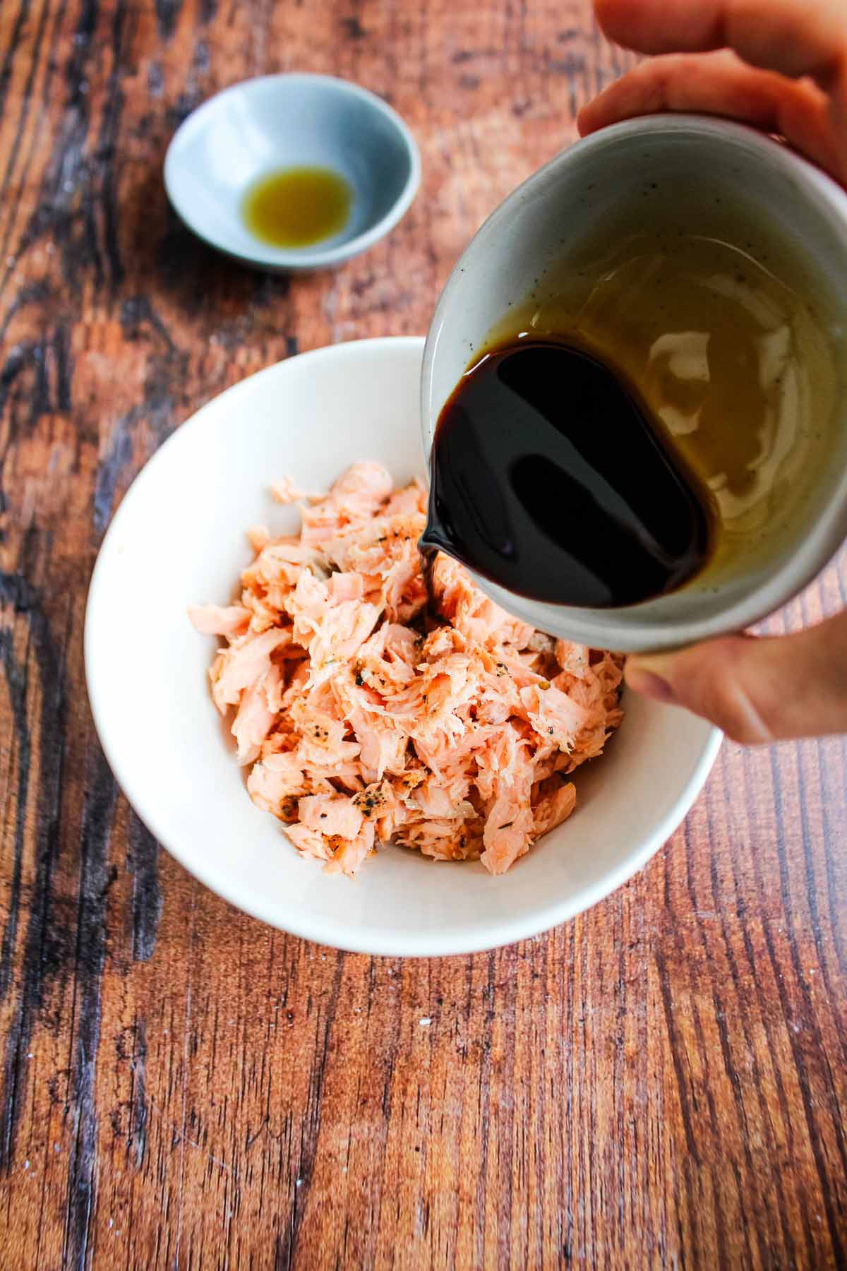 Adding soy sauce and seasonings to salmon in a bowl.