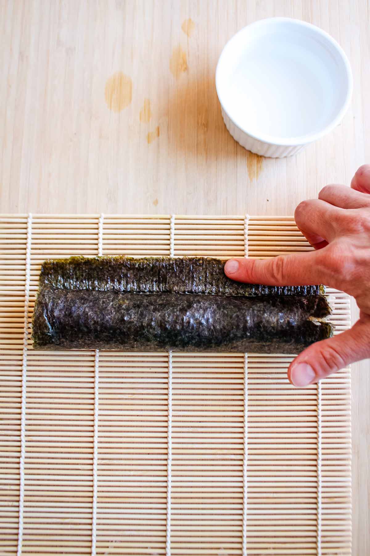 Dampening the edge of the nori sheet before finishing wrapping.