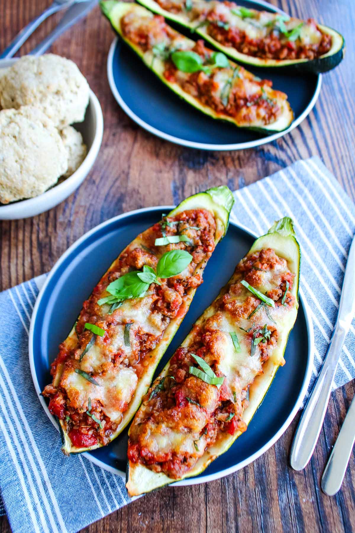 Ground turkey zucchini boats two plates on the table with a bowl of rolls.