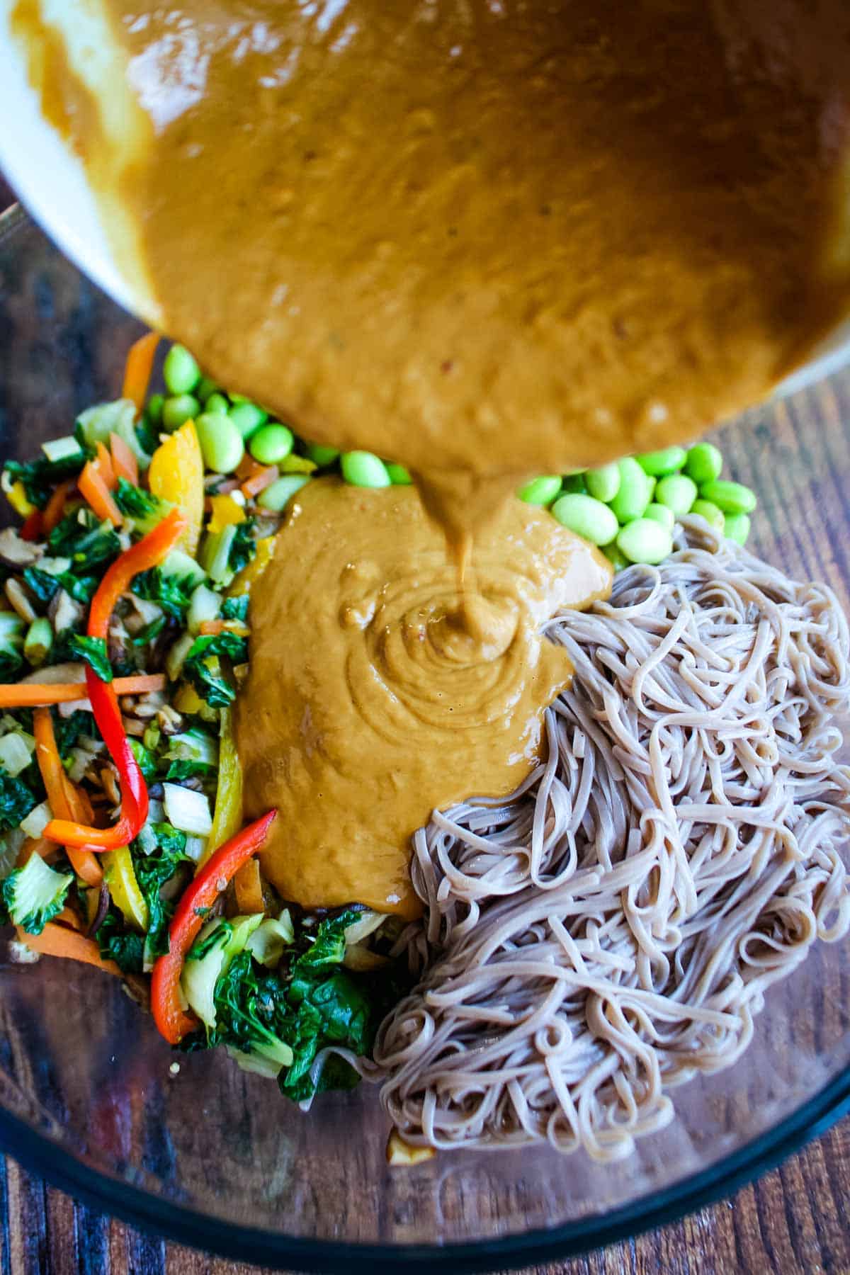 Adding peanut sauce to the noodles and veggies.