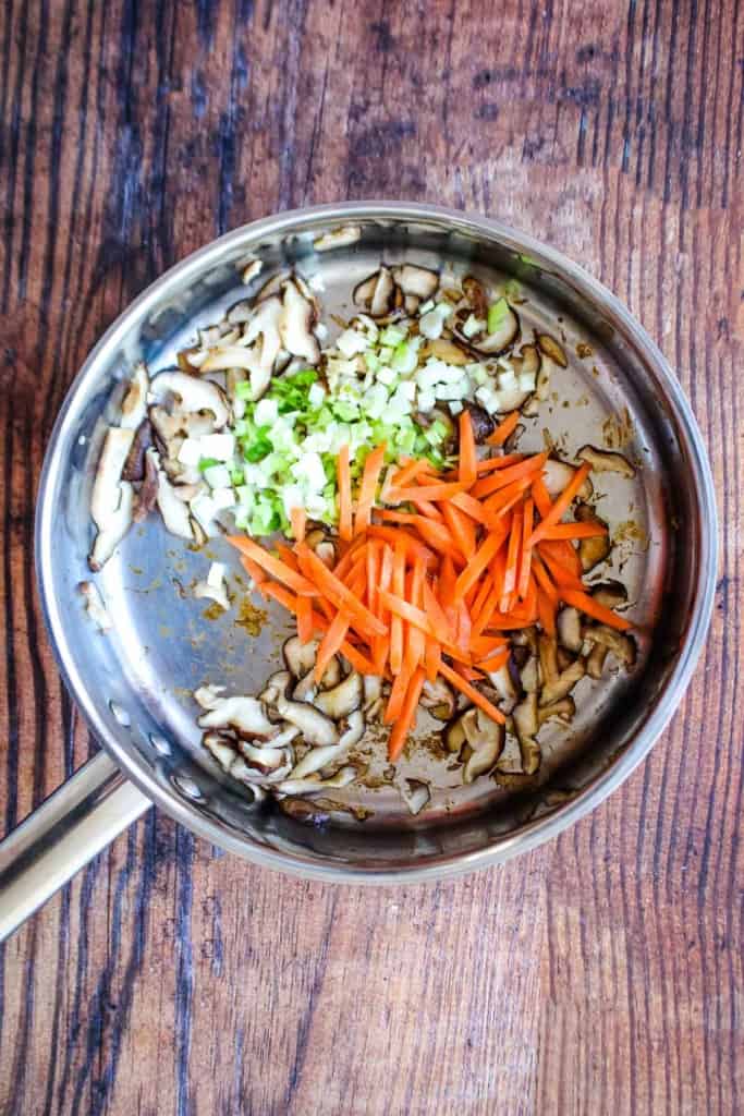 Green onions and grated carrots added to the skillet.