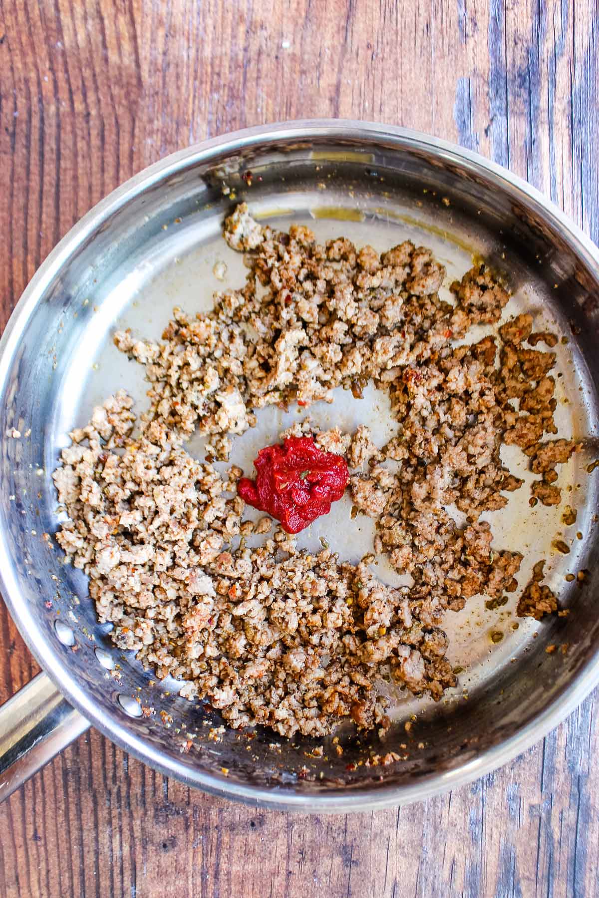 Sausage crumbles in a skillet with tomato paste.