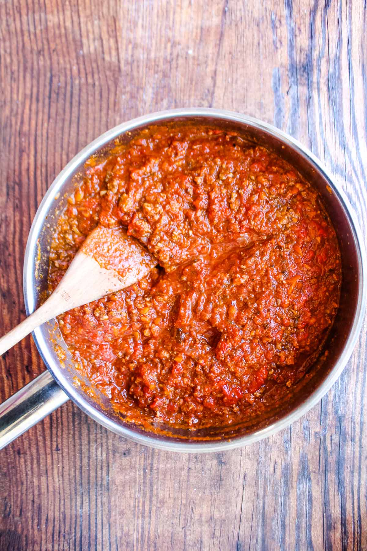 Italian sausage bolognese in a skillet with wooden spoon.