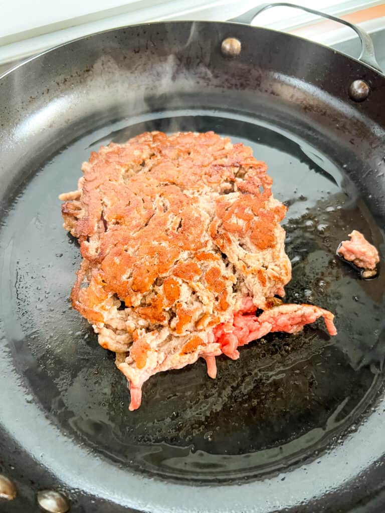 Ground pork browning in a pan, with the cooked side up.