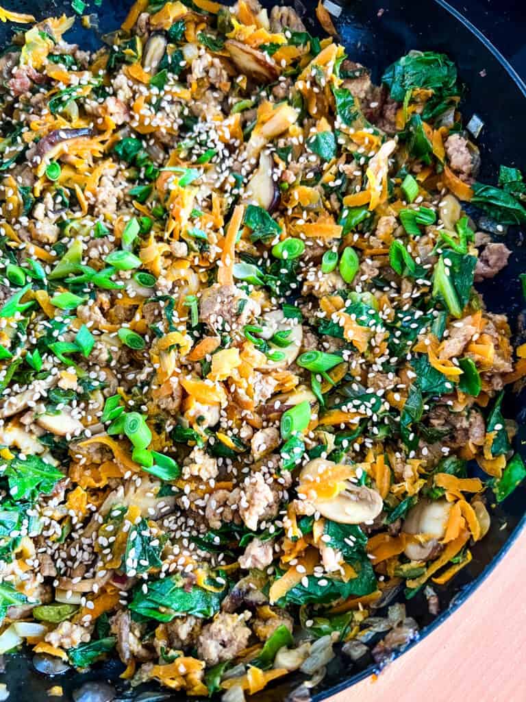 Finished stir fry in skillet with cooked vegetables and ground pork, topped with sesame seeds and green onions.