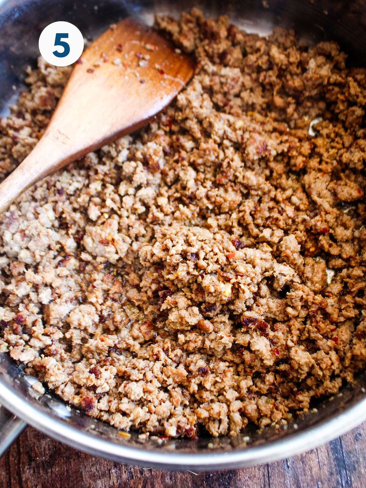 Cooked ground pork in a skillet with a wooden spoon after the meat is cooked.