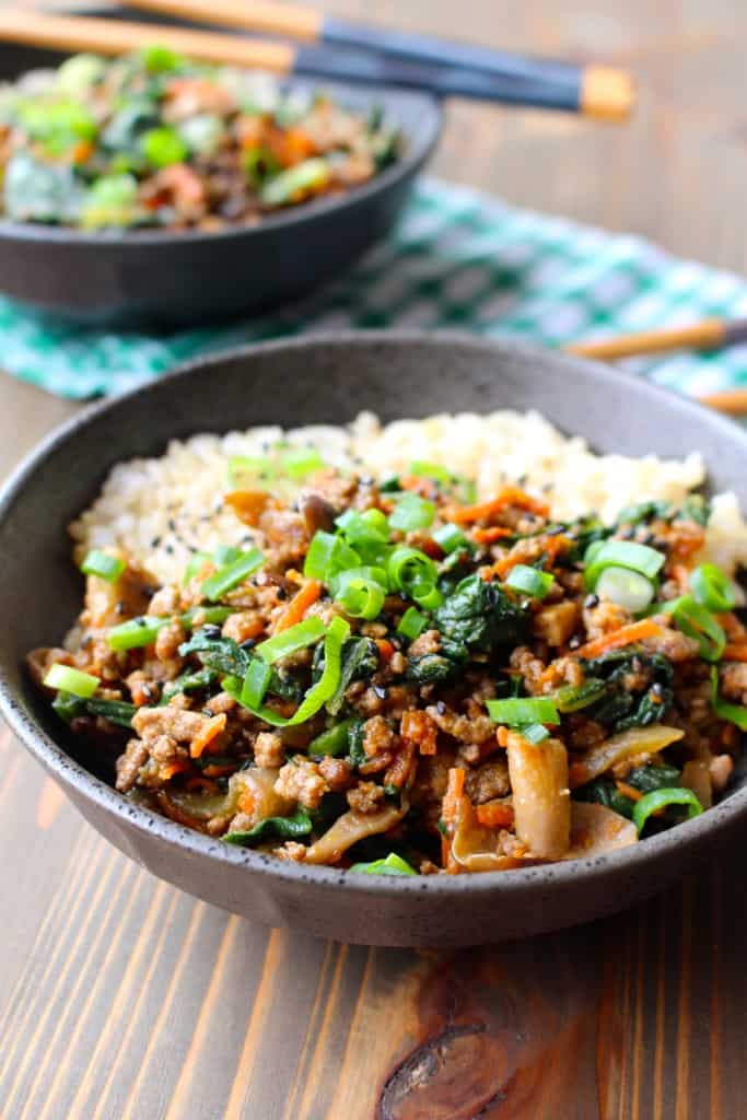 dark slate bowl with brown rice and mixed stir fry topped with green onions.