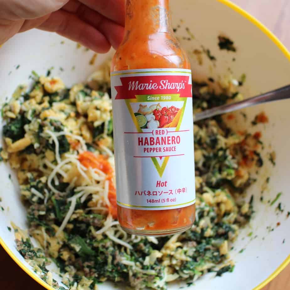 Breakfast Calzones filling in a bowl with red habanero pepper sauce in a bottle in the foreground