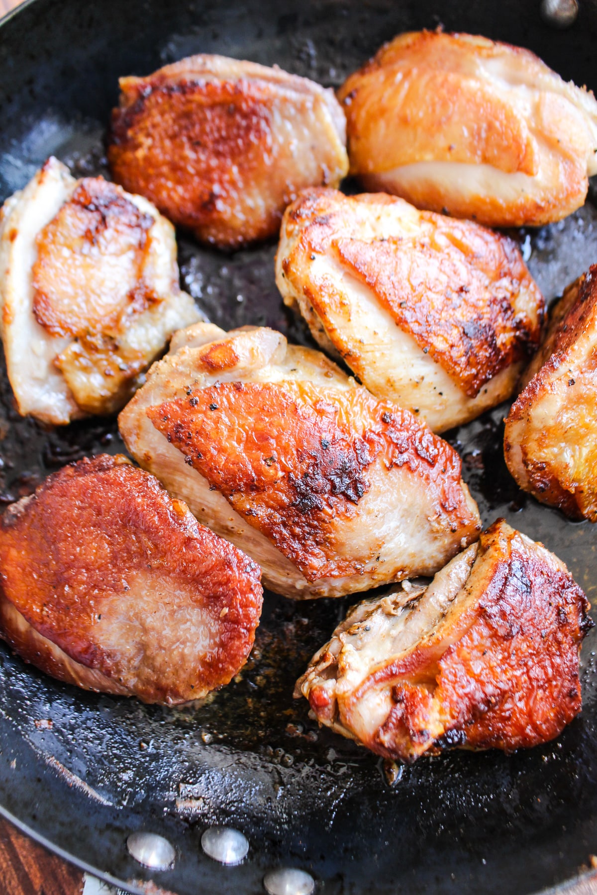 Chicken thighs flipped over and cooking on the other side in a skillet.