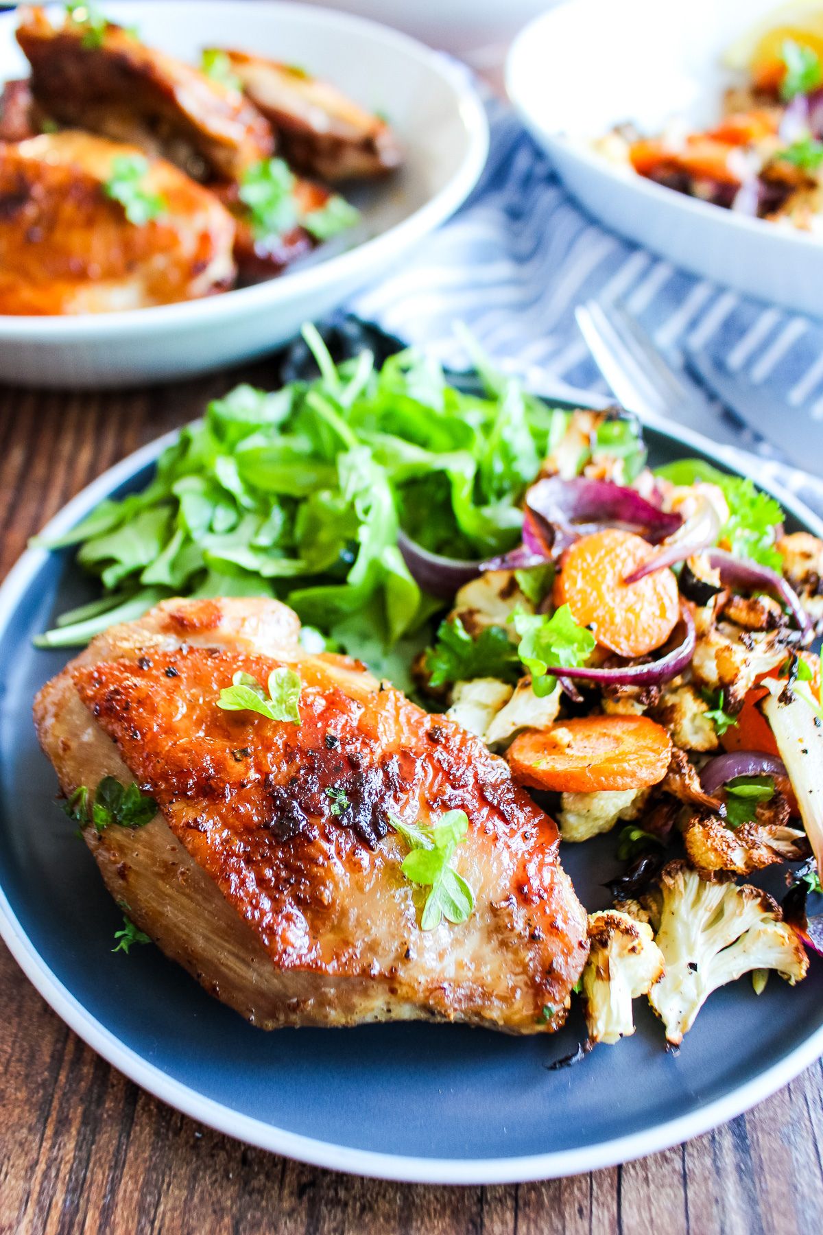 Cast iron chicken thighs on a blue plate on the table with salad and vegetables.