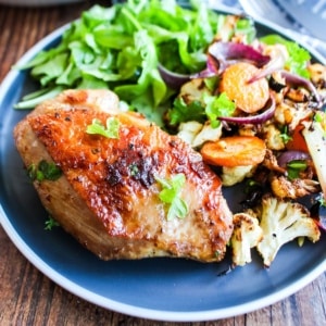 Cast iron chicken thighs served up on a blue plate with sides.