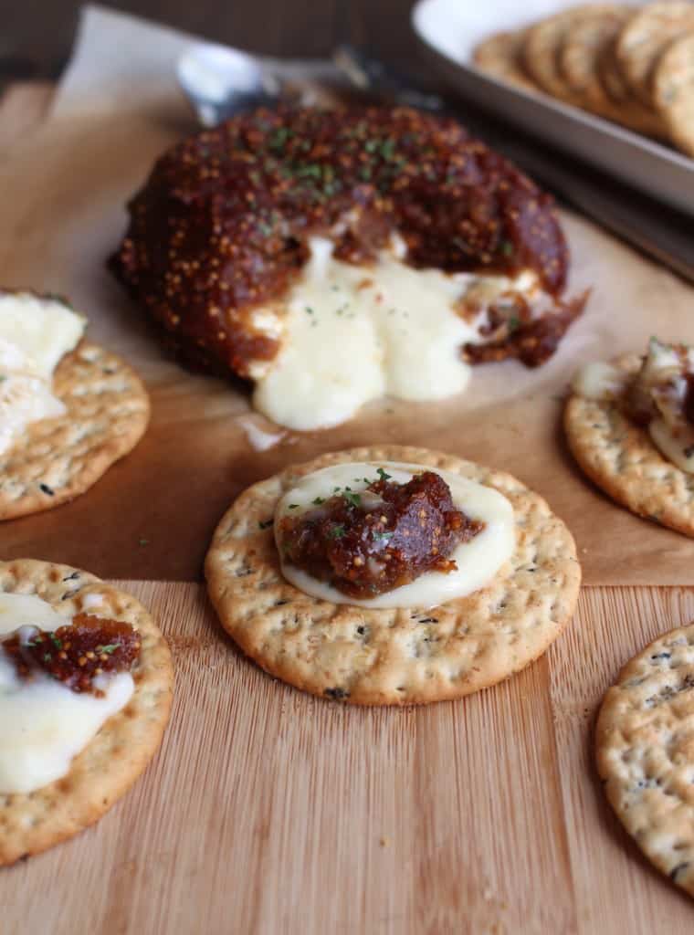 a rind of fig baked brie on a baking sheet surrounded by crackers with brie and fig