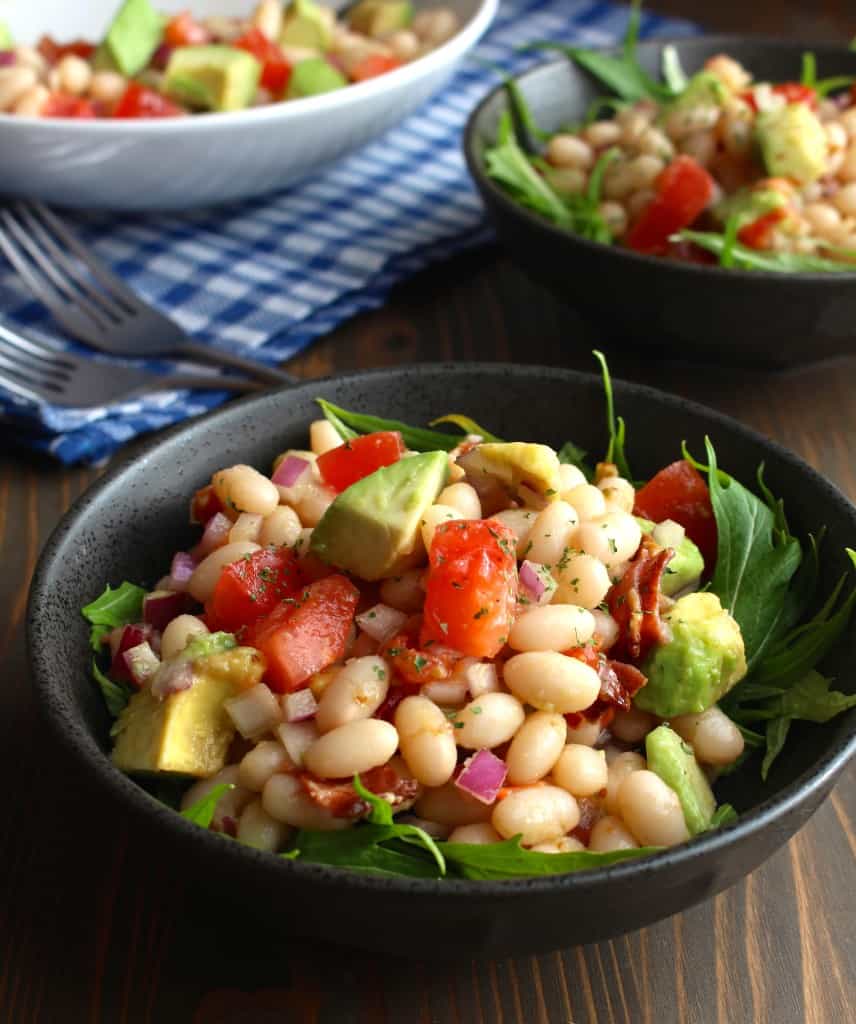 avocado with white beans, bacon, and tomatoes in bowls on a picnic table