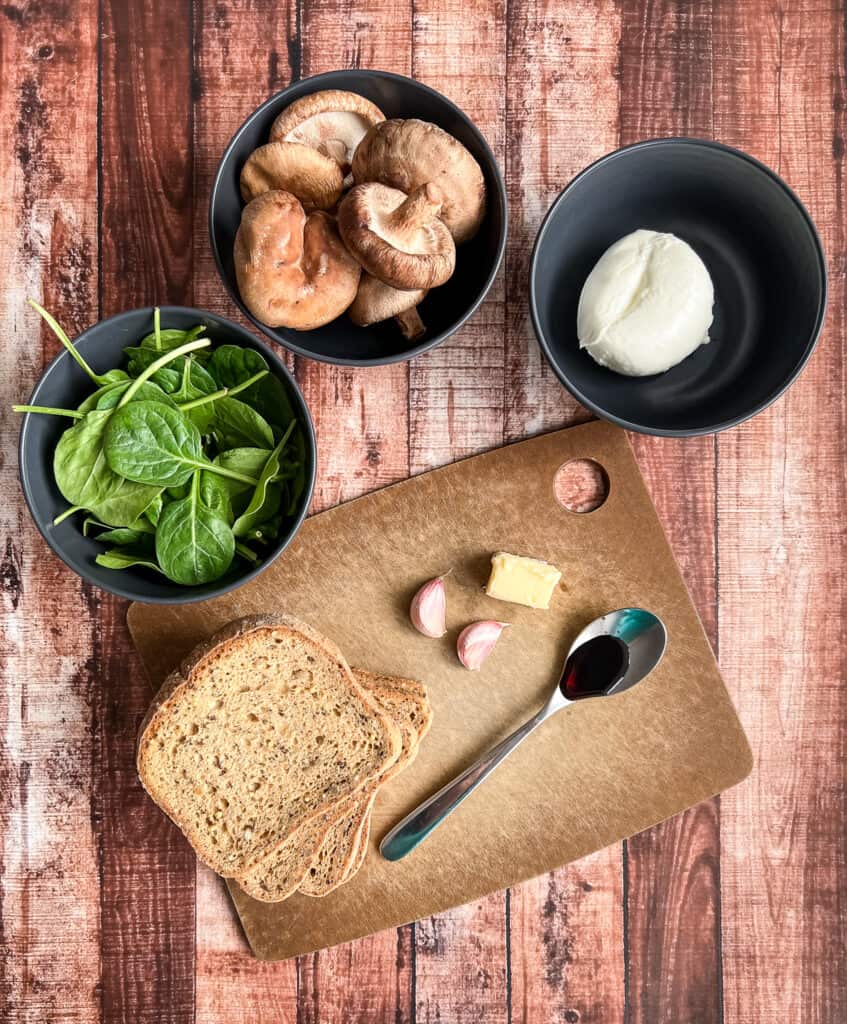 Mushrooms, cheese, spinach, bread, butter, and garlic on a table to make a grilled cheese.