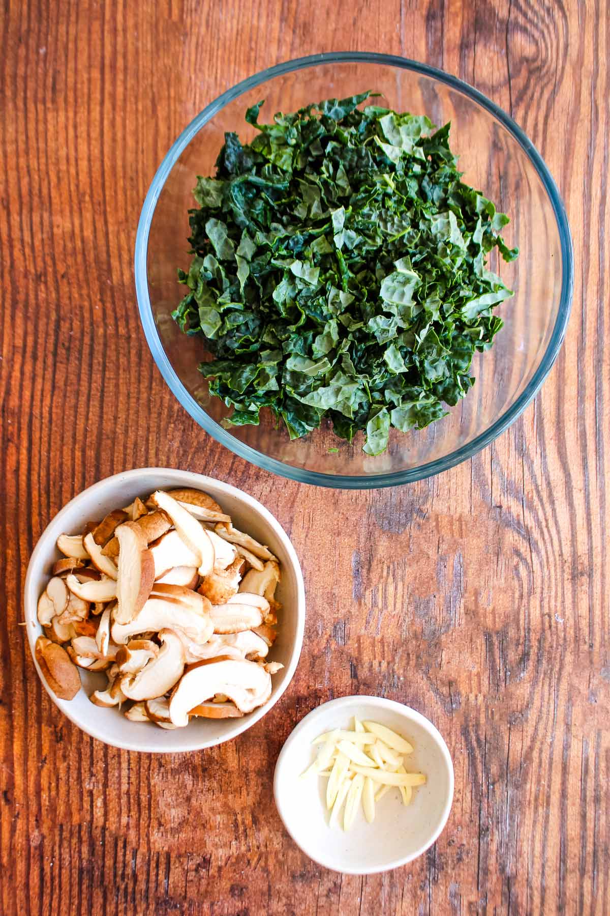 Bowl of chopped kale, sliced mushrooms and chopped garlic on the table.
