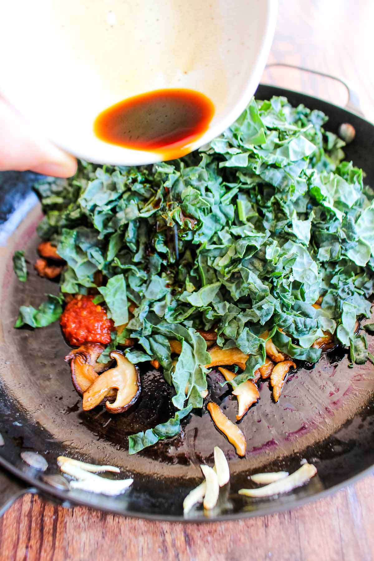 Adding the greens and soy sauce to the mushrooms.