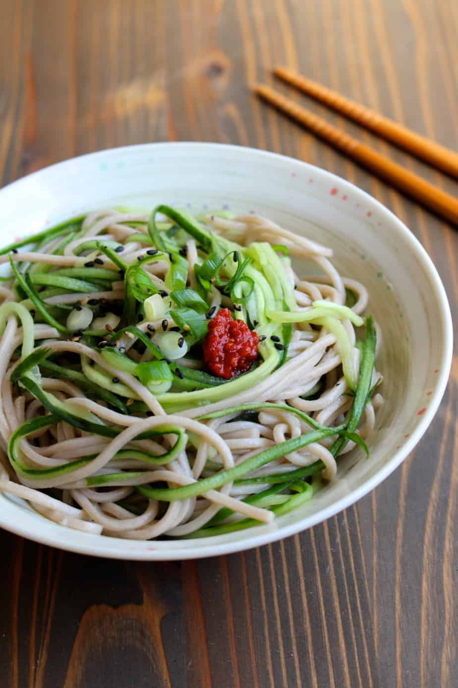 Cucumber noodle soba salad in a white bowl with chopsticks 