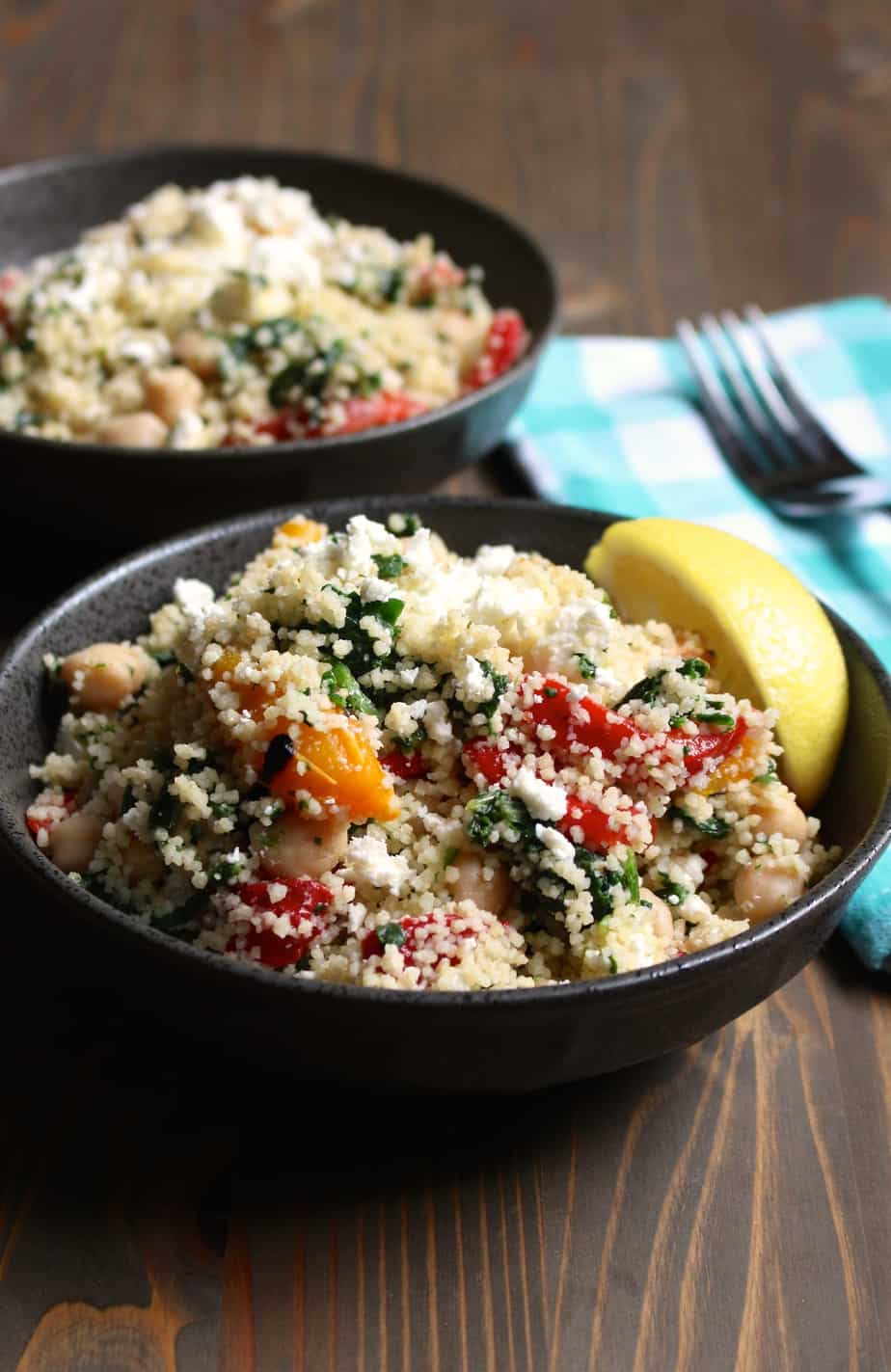 Easy lemony feta couscous with spinach in a black bowl with additional veggies mixed in