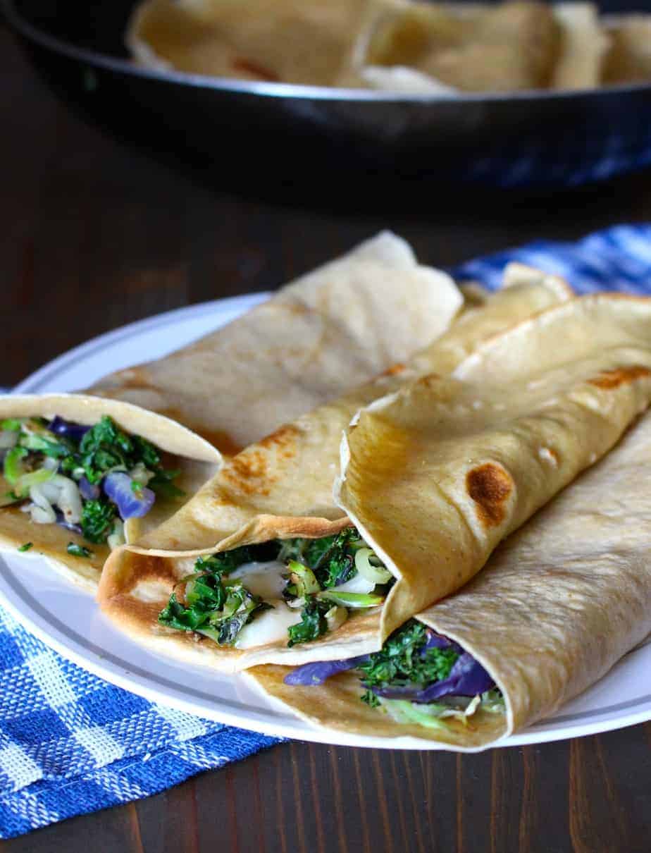 Three kale and white cheddar crepes on a white plate