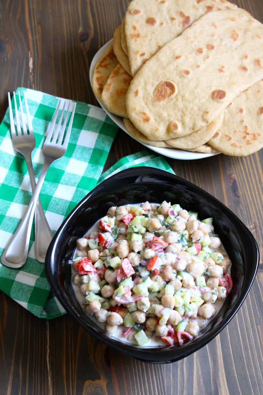 Chickpea tzatziki salad in a black bowl beside a plate of naan