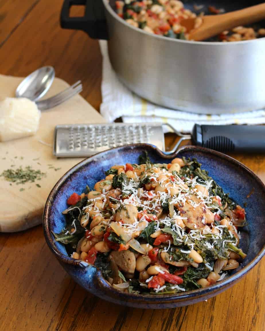 One pot recipe of sausage, white beans, and kale in a bowl with the cooking pot sitting out of focus in the background