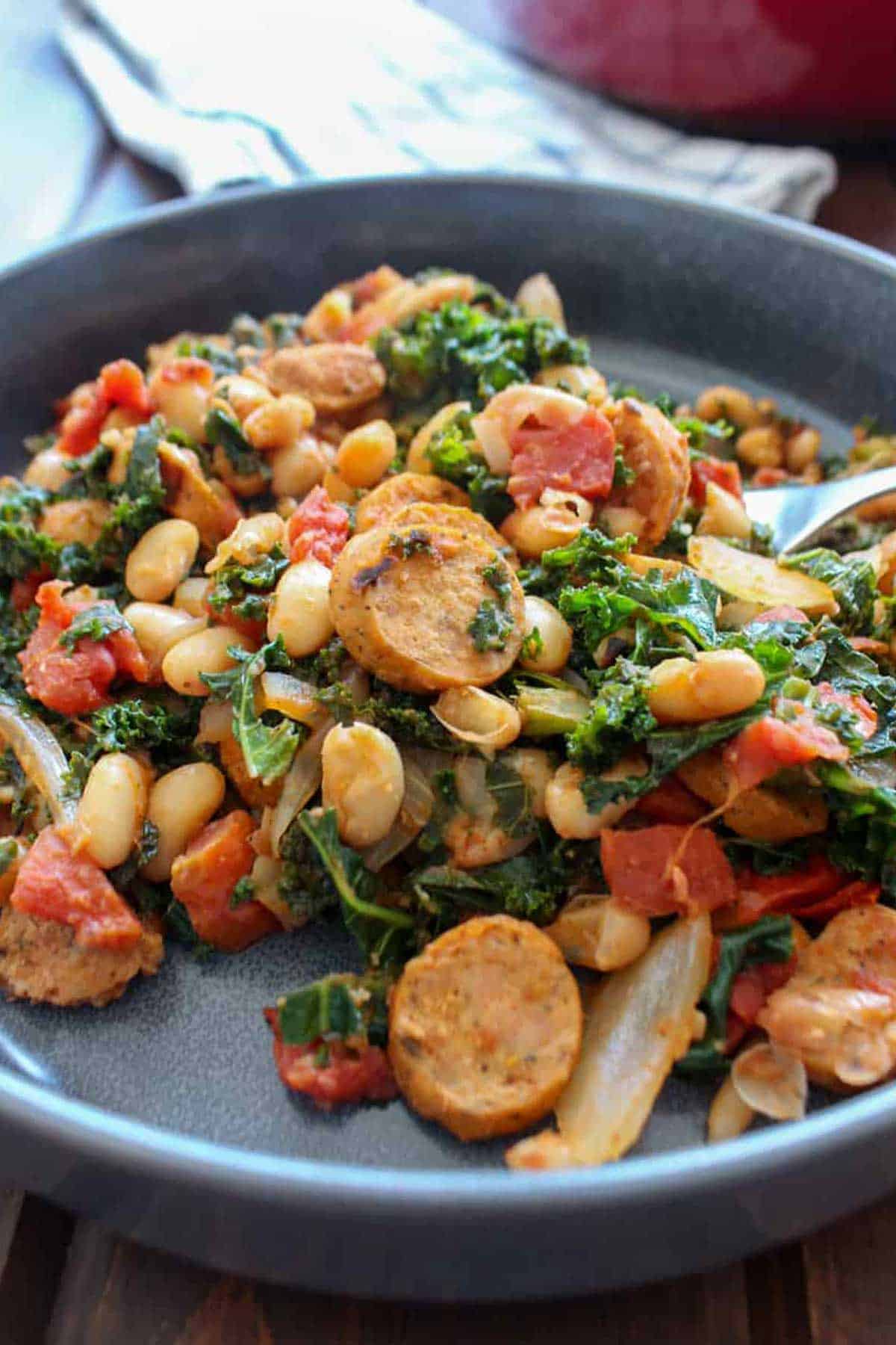 A plate of white bean and sausage skillet with a fork digging into it.
