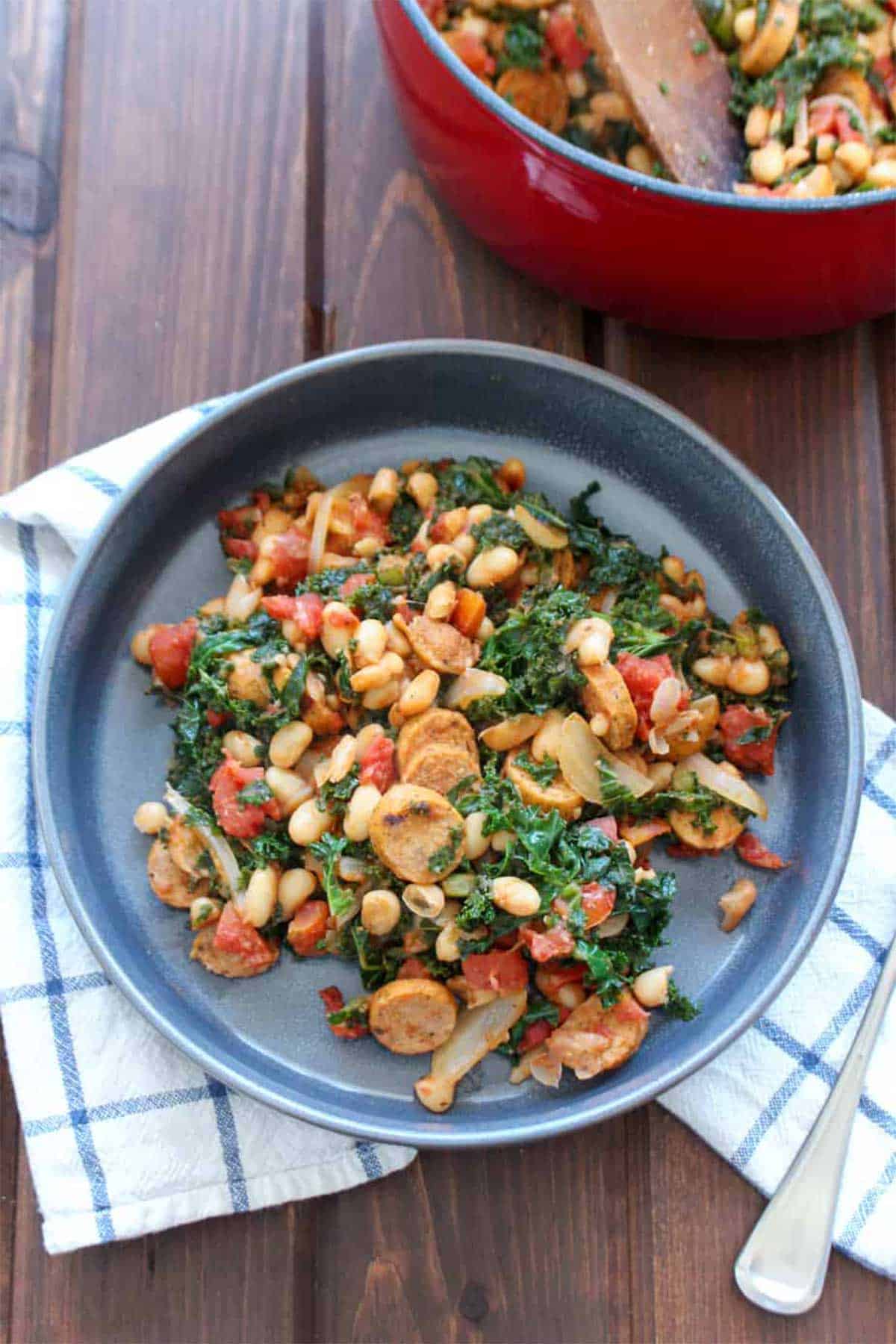 Sausage and beans with kale served up on a blue plate on the table.